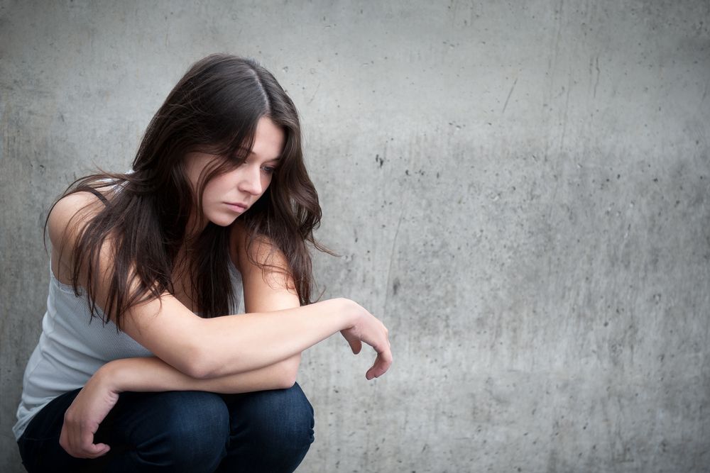 A teenage girl sits looking sad or in pain.