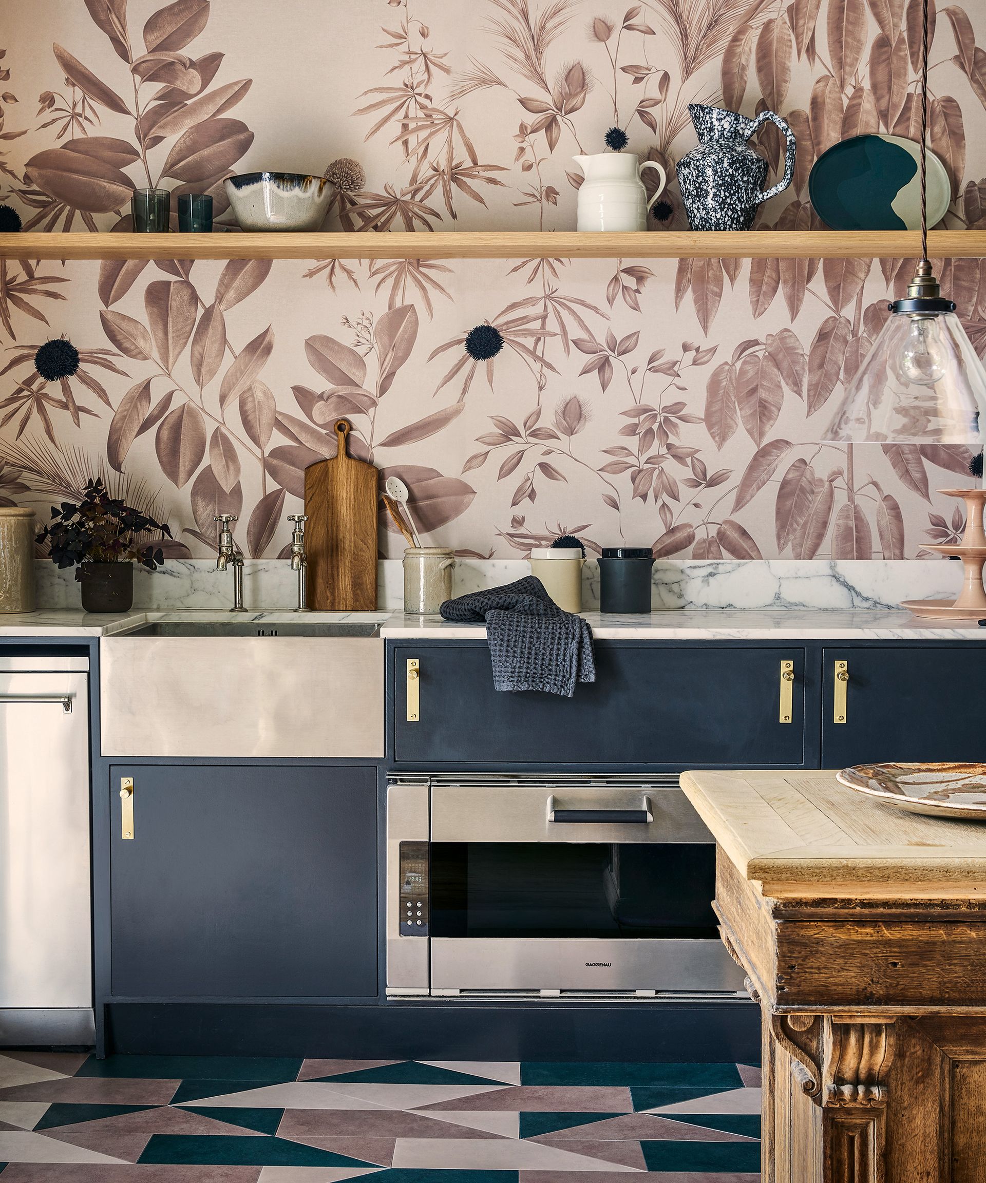 A kitchen with pink floral wallpaper, blue cabinets and a geometric tiled floor
