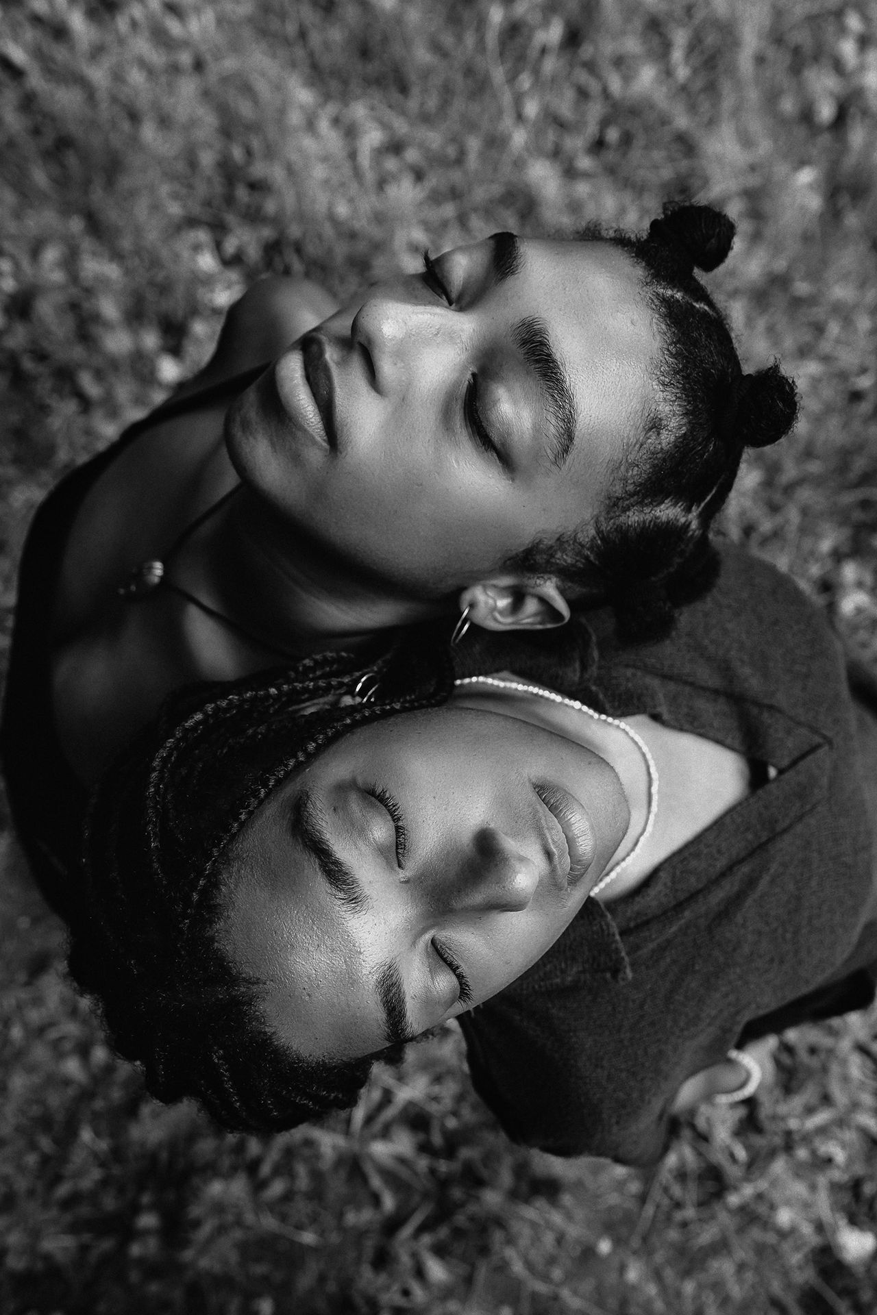 Two women are entwined, standing next to each other, head up and eyes closed, surrounded by a nature backdrop in a monochromatic tone