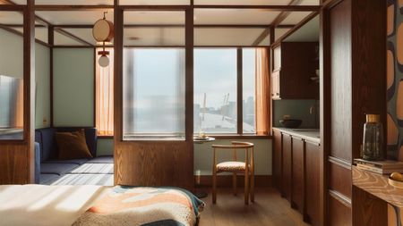A sun-lit hotel suite with colorful bedsheets in pastel tones and deep seating pale blue banquettes, decorated with vaguely Japanese-reminiscent wooden and paper detailing throughout.