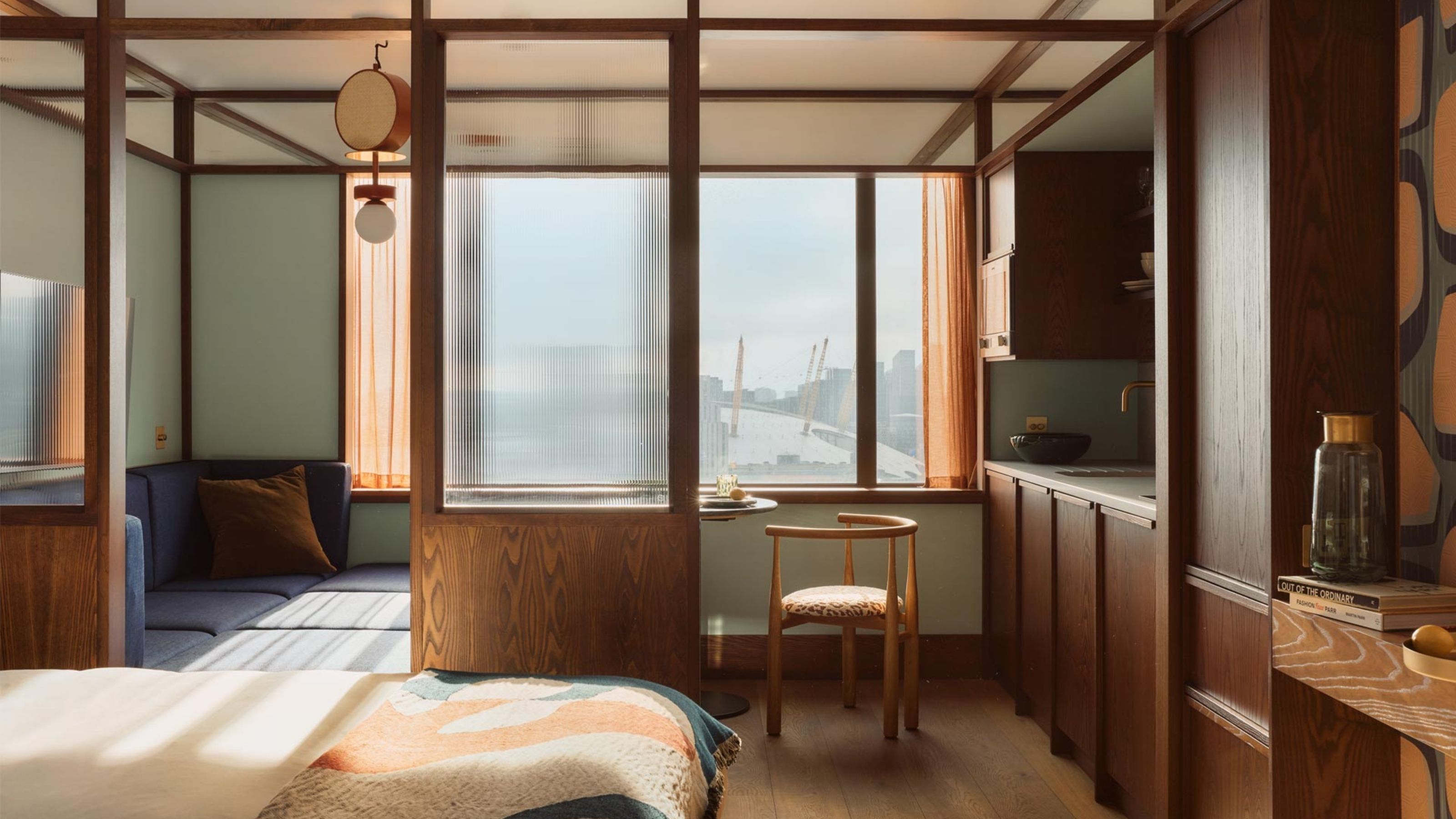 A sun-lit hotel suite with colorful bedsheets in pastel tones and deep seating pale blue banquettes, decorated with vaguely Japanese-reminiscent wooden and paper detailing throughout.