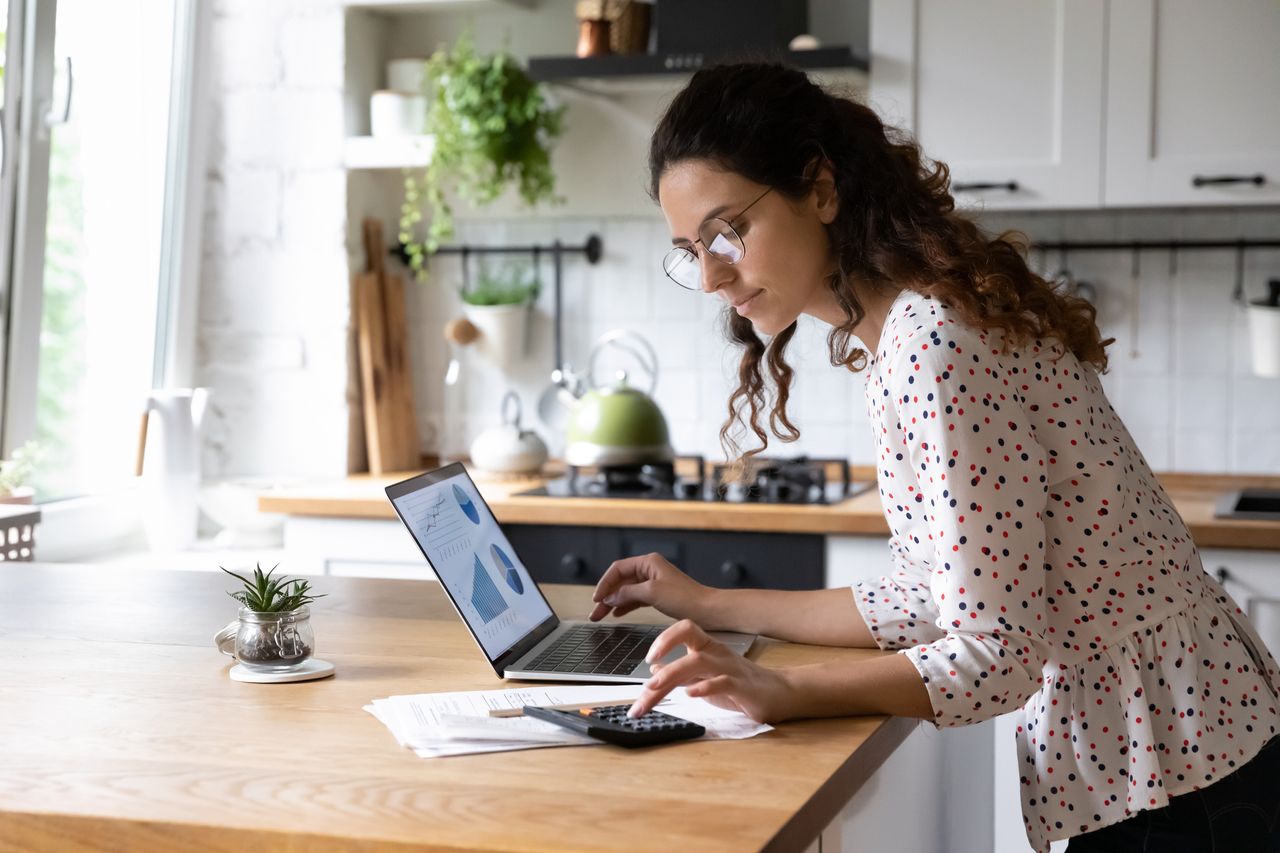 Woman at kitchen table with laptop and calculator