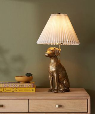A bronze gold table lamp on a wooden table with a green wall