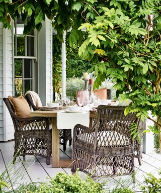 An example of outdoor dining ideas showing a dining table with large, dark rattan chairs surrounded by foliage
