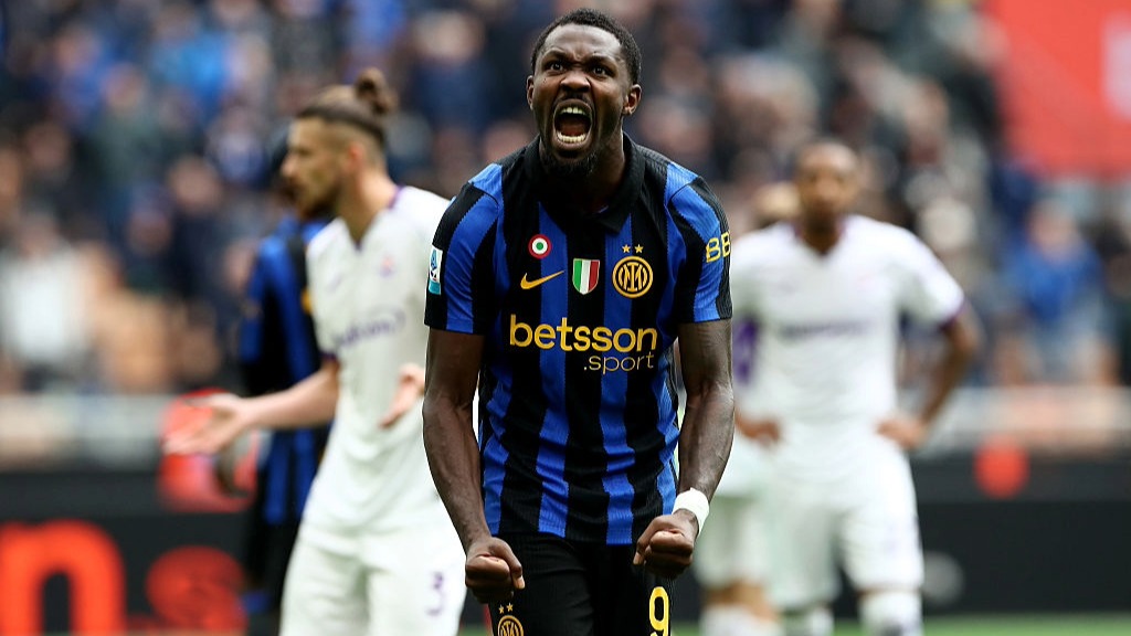 Marcus Thuram, wearing Inter Milan's black and blue kit, tenses his shoulders and shouts in celebration after scoring a goal.