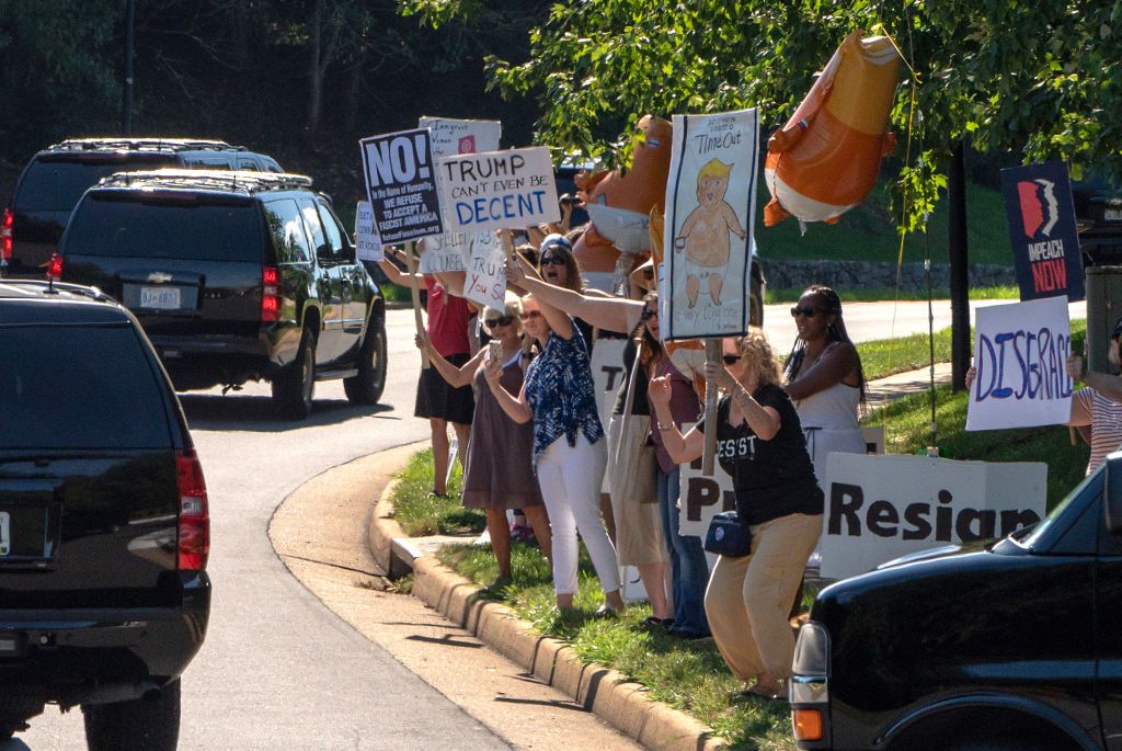 Protesters hold signs along Trump motorcade route