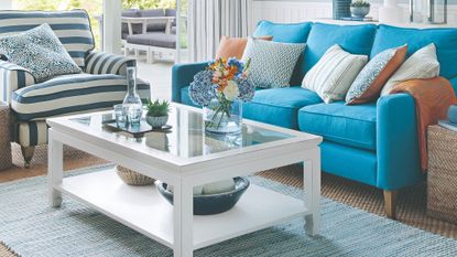 Living room with sofa in bright blue, pale blue walls, rug in pale blue, white ceiling and white table