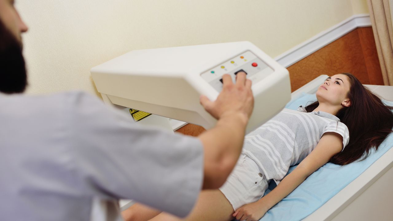 The doctor examines a young woman on a DEXA scan