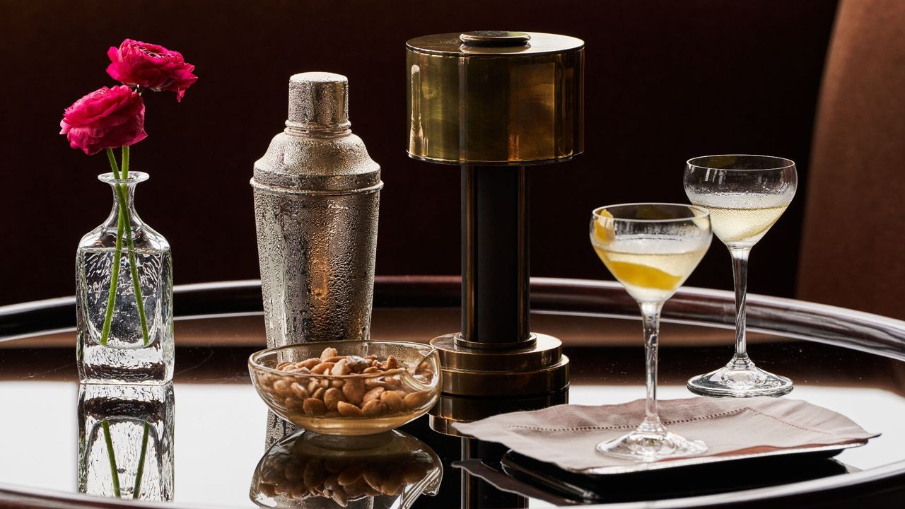 Cocktails, a lamp, bowl of nuts, cocktail shaker and vase of flowers on a table