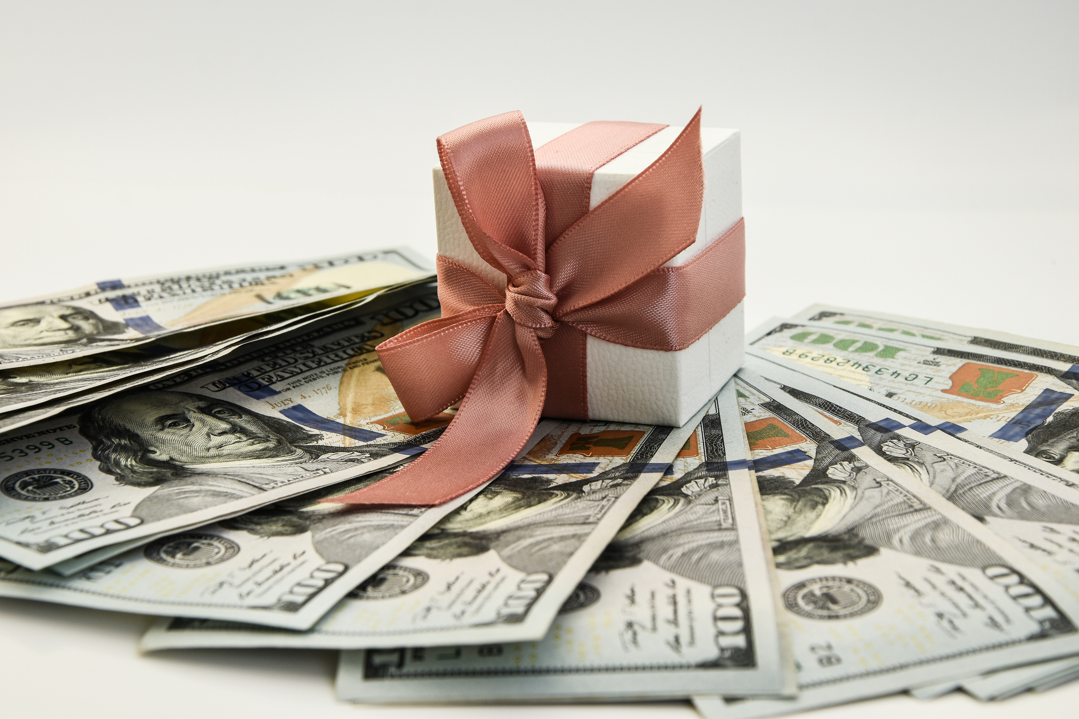 US money underneath a wrapped gift with a bow on top