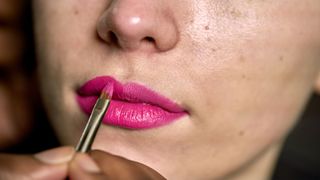 woman applying pink lipstick with brush