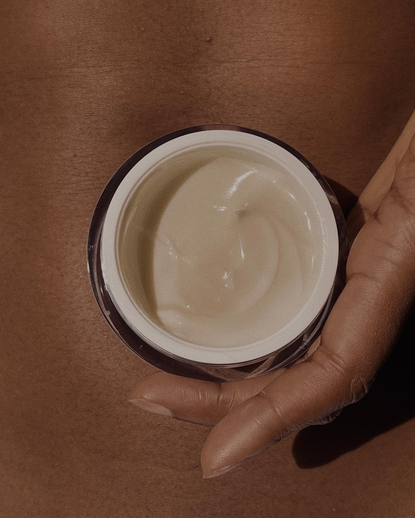 A hand holding a round pot of body lotion