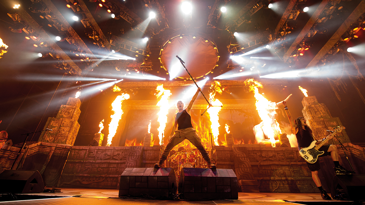 A photograph of Bruce Dickinson on stage with fire behind him