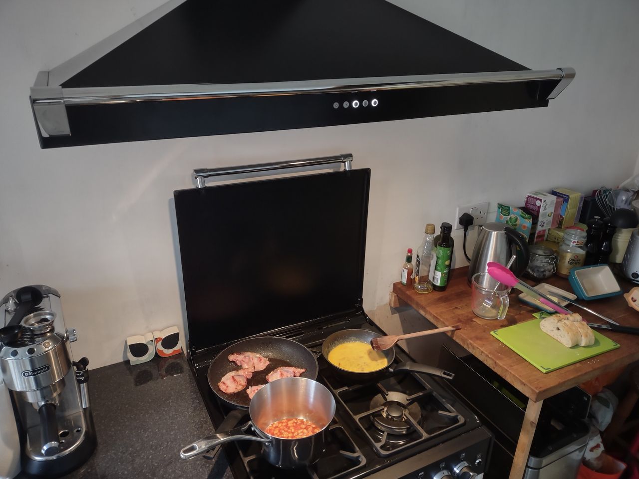 Food being cooked on a black hob with a black pyramid chimney cooker hood extracting air above the pans