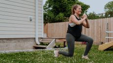 Woman exercises in yard next to house. She smiles as she performs a lunge