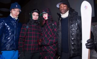 Four models, one wearing a blue shiny jacket, two with black and red plaid jackets and one in a black jacket