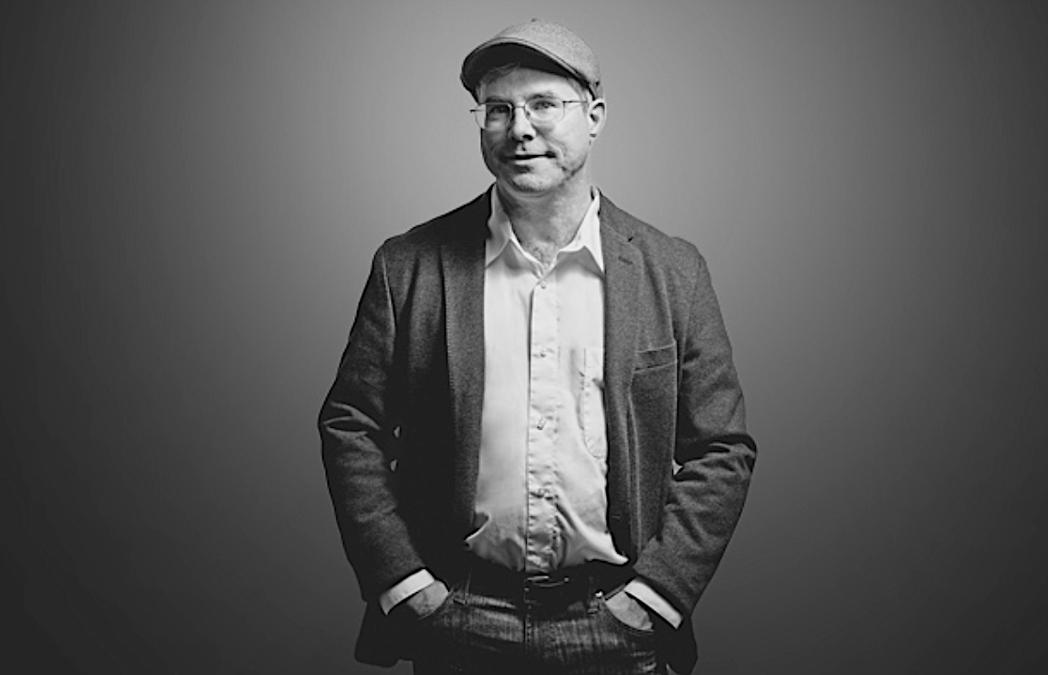 A black-and-white portrait of a man in a sport coat and cap