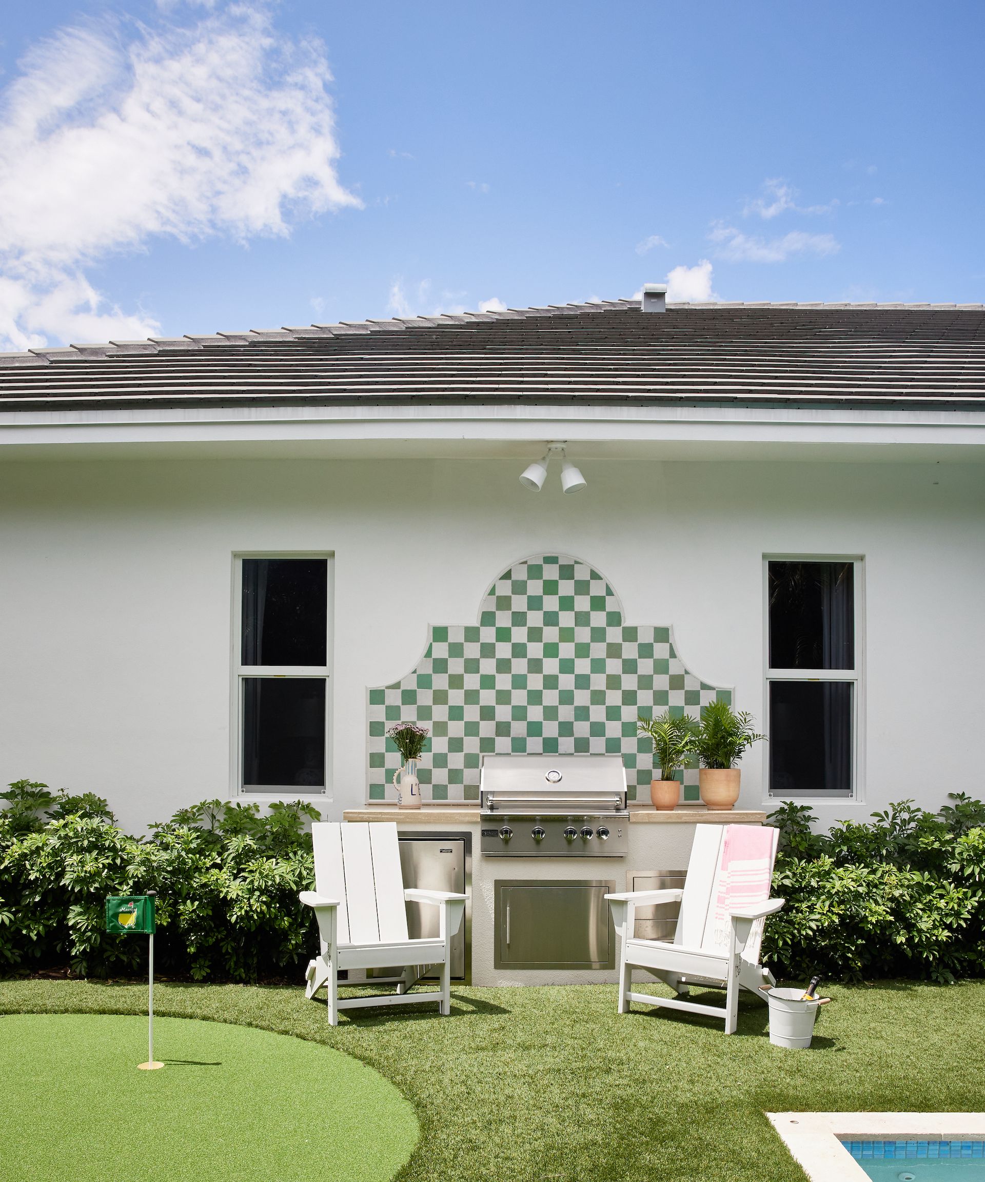 Outdoor kitchen with green and white checked backsplash and stainless steel grill with two chairs in front
