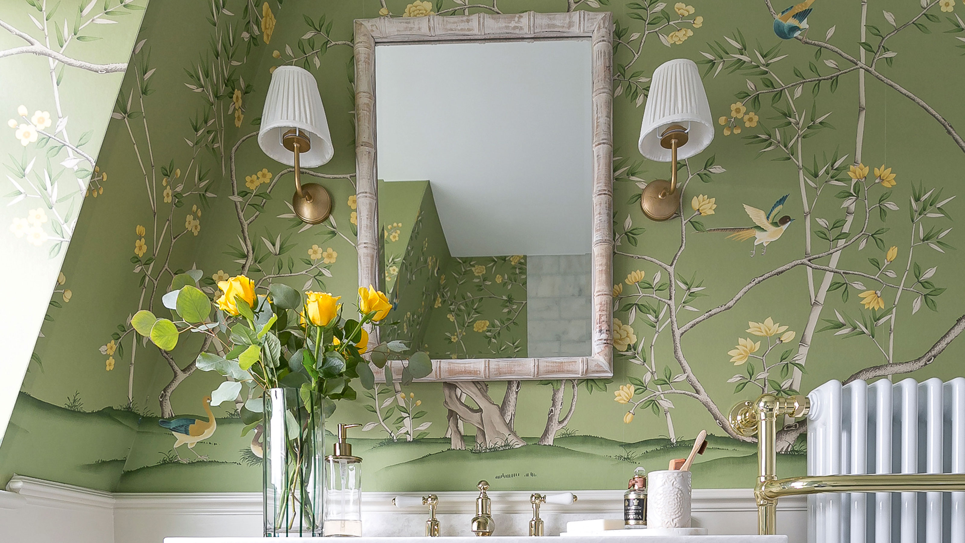 Green floral wallpaper with white vanity cabinet and bamboo mirror with wall lights