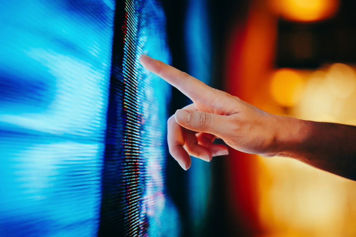 Close up of woman&#039;s hand touching illuminated and multi-coloured LED display screen.