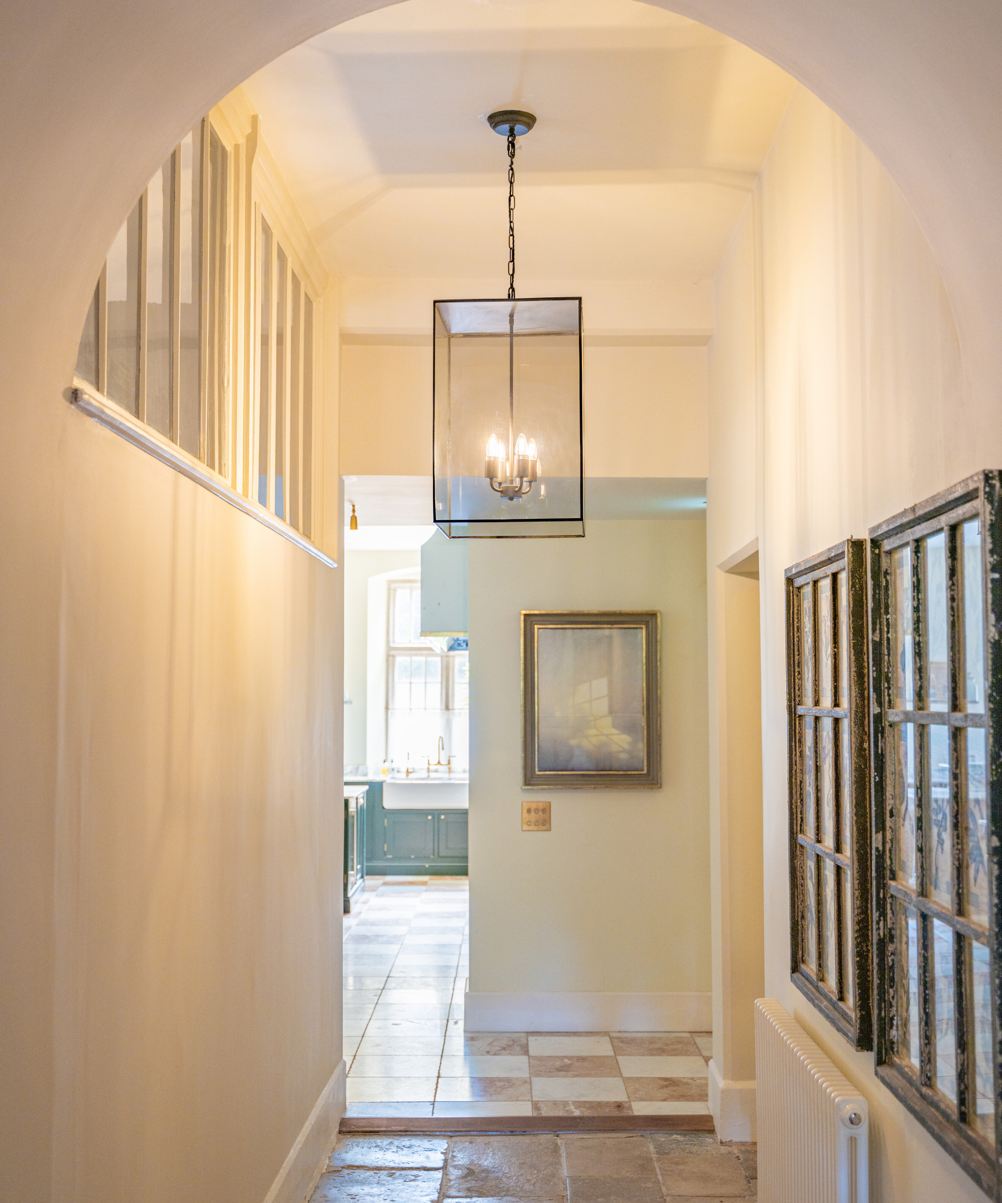 narrow hallway with high ceiling, rectangular glass and metal shade, rectangular high level internal windows and cupboards below