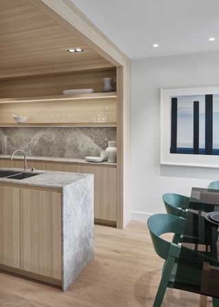 Green dining table chairs on the right and on the left of the kitchen is a large stone island with the same stone used across the kitchens countertop and backsplash.