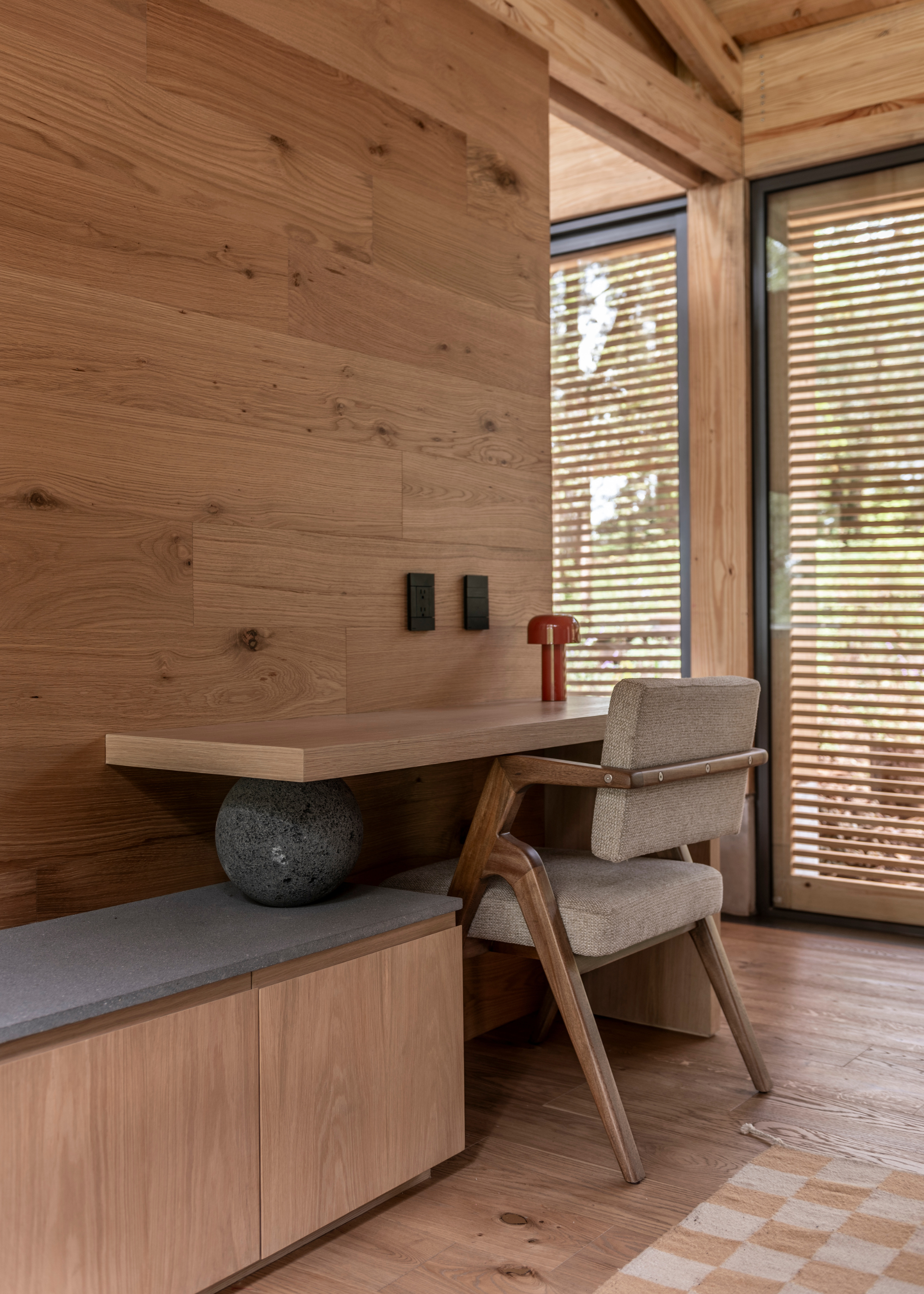 A study space with a wood table, a checkerboard rug and a red table lamp