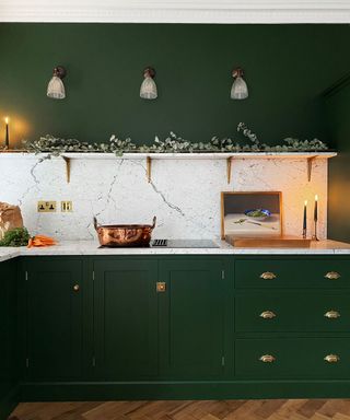 Green Kitchen cabinets, parquet floors, white stone counters with glass stove, copper pot, open shelving, green walls and wood chopping board