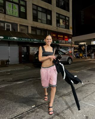 lucy wears basketball shorts, black crop top, and heels