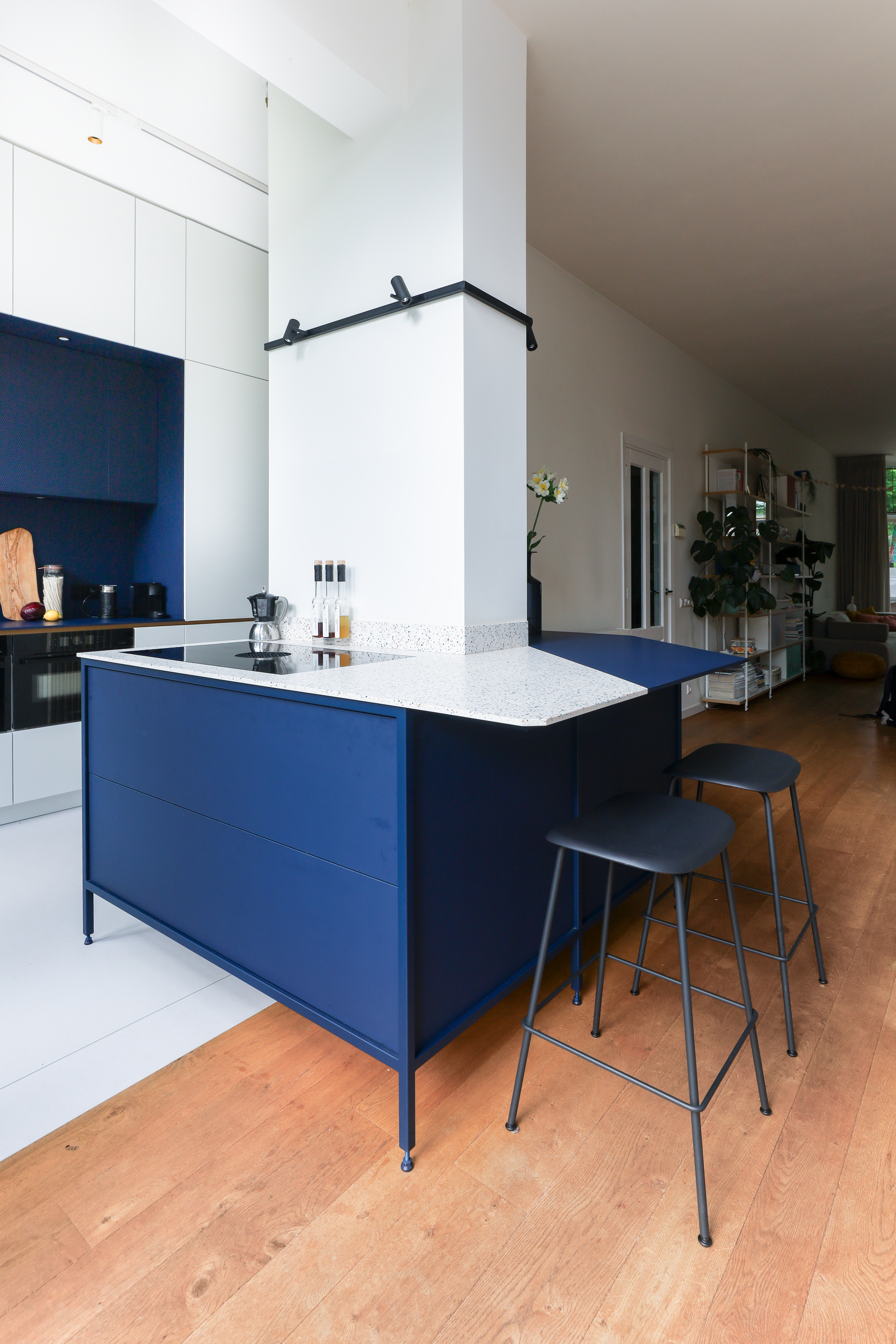 A kitchen with white walls, and an island designed on a column, in two tones of white and navy blue
