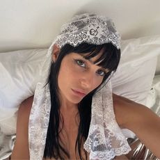 An image of a woman with winged eyeliner and bangs wearing a lace scarf over her head.