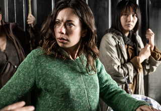 Anna Castillo as Mia with some other fleeing civilians in the background