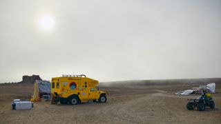 The sun is just visible through clouds above a dry Arctic base camp.