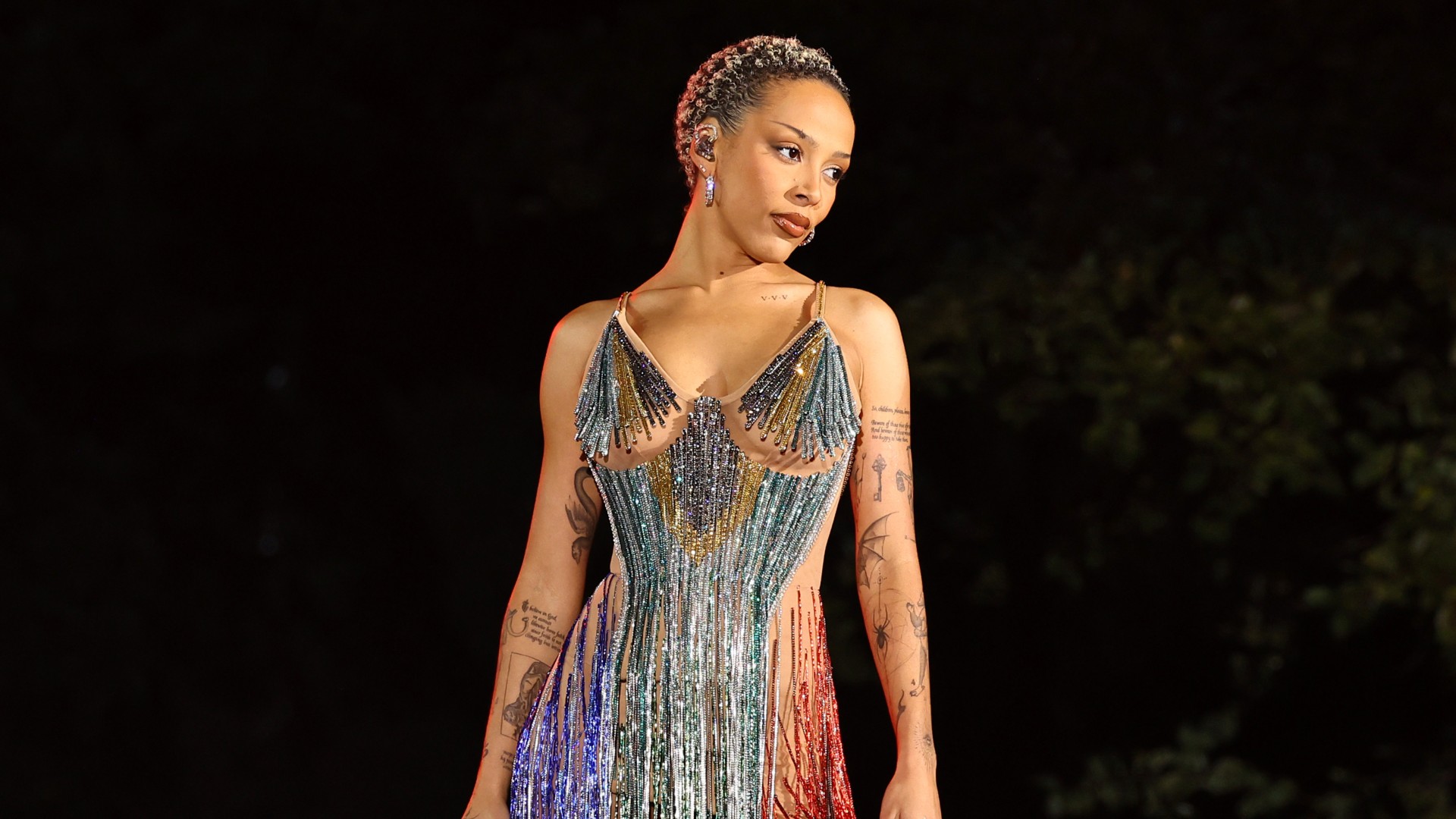 a woman with short hair standing on a stage wearing a short, sparkly dress with tassels