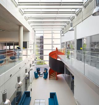 Inside the Institute, a first floor view overlooking a white-spacious seating area with a spiral staircase and glass windows