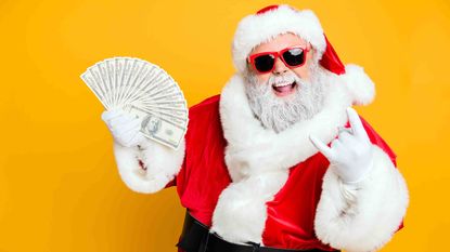 A Santa Claus in sunglasses holding a fan of 100-dollar bills and flashing a rock sign