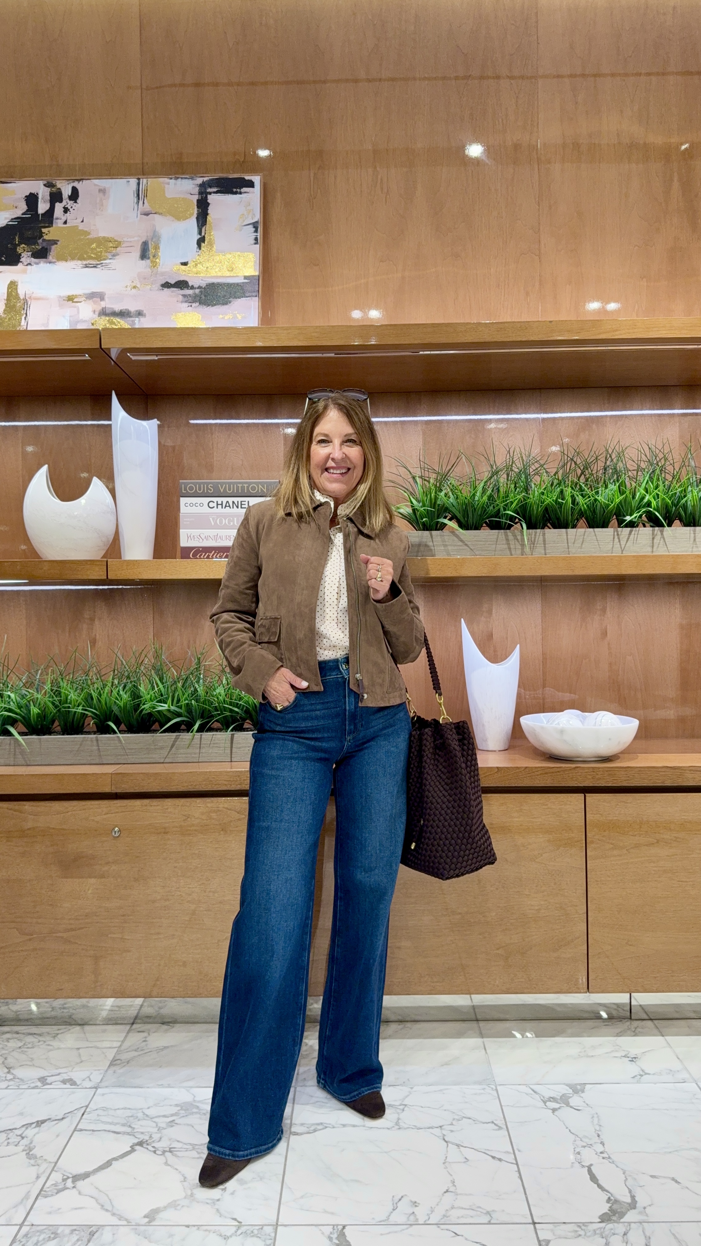 Sandy Koszarek wearing a tan jacket, a white top, jeans, and boots.