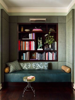 sofa with bookcase behind with textured pale green wallcovering and dark wood floor with small round coffee table
