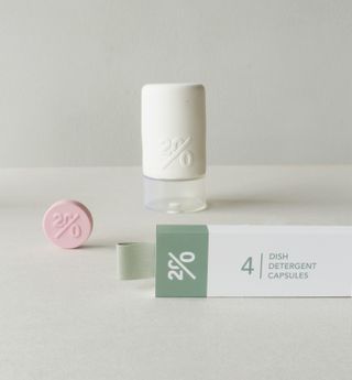 A white and green box of dish detergent capsules, with a pink capsule standing next to it.