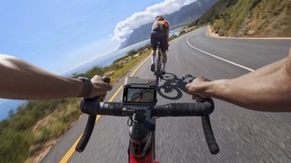 La Insta360 Ace Pro 2 con la pantalla inclinada hacia arriba y acoplada a una bicicleta de carretera que circula a gran velocidad por una soleada carretera costera.