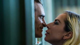 Arthur Fleck (Joaquin Phoenix) and Harley Quinn (Lady Gaga) kissing between prison bars in Joker: Folie a Deux