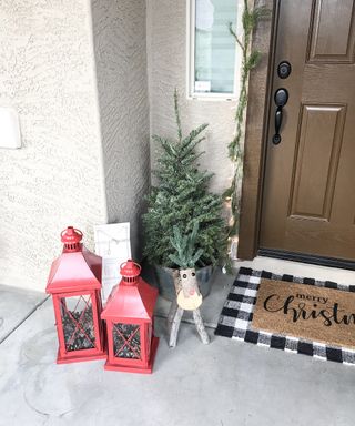 Christmas porch decor with red lanterns filled with pinecones wooden reindeer festive door mat and Christmas tree