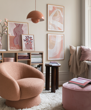 A pink living room with accent chairs and pink and red themed art prints