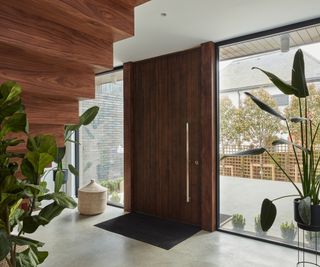 large walnut door with long chrome handle in modern setting with walnut stairs and large glass black framed panels either side of door