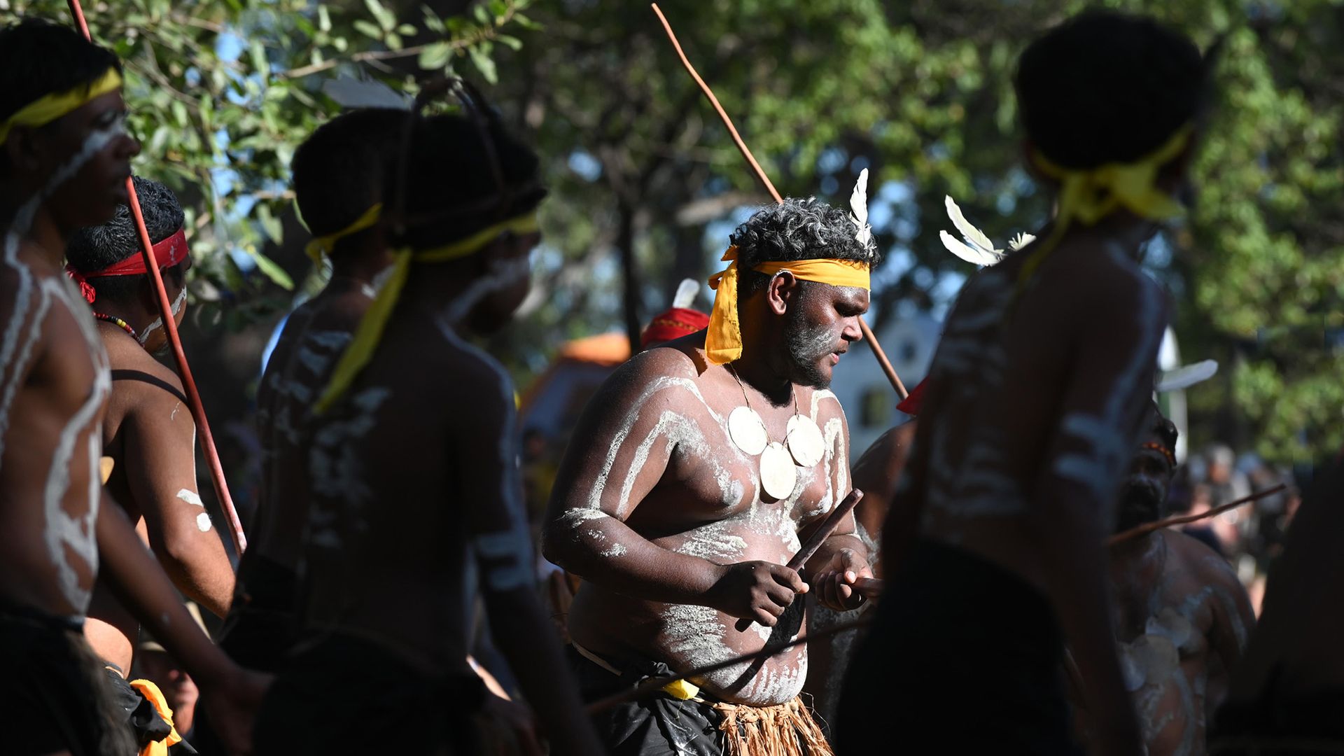 A group of people wearing feathers and skirts dance around.