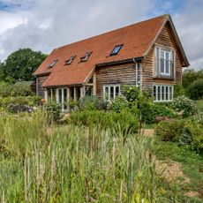  Exterior of a timber clad, oak framed house with lawn and flower beds. A new build oak framed two bedroom house in the New Forest in Hampshire, home of Elizabeth and Derek Sandeman