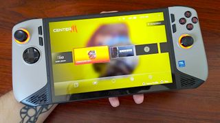 Hand holding MSI Claw 8 AI+ in front on woodgrain desk with CentreM software on screen.