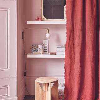 Pink dressing table built into wall with red curtain.