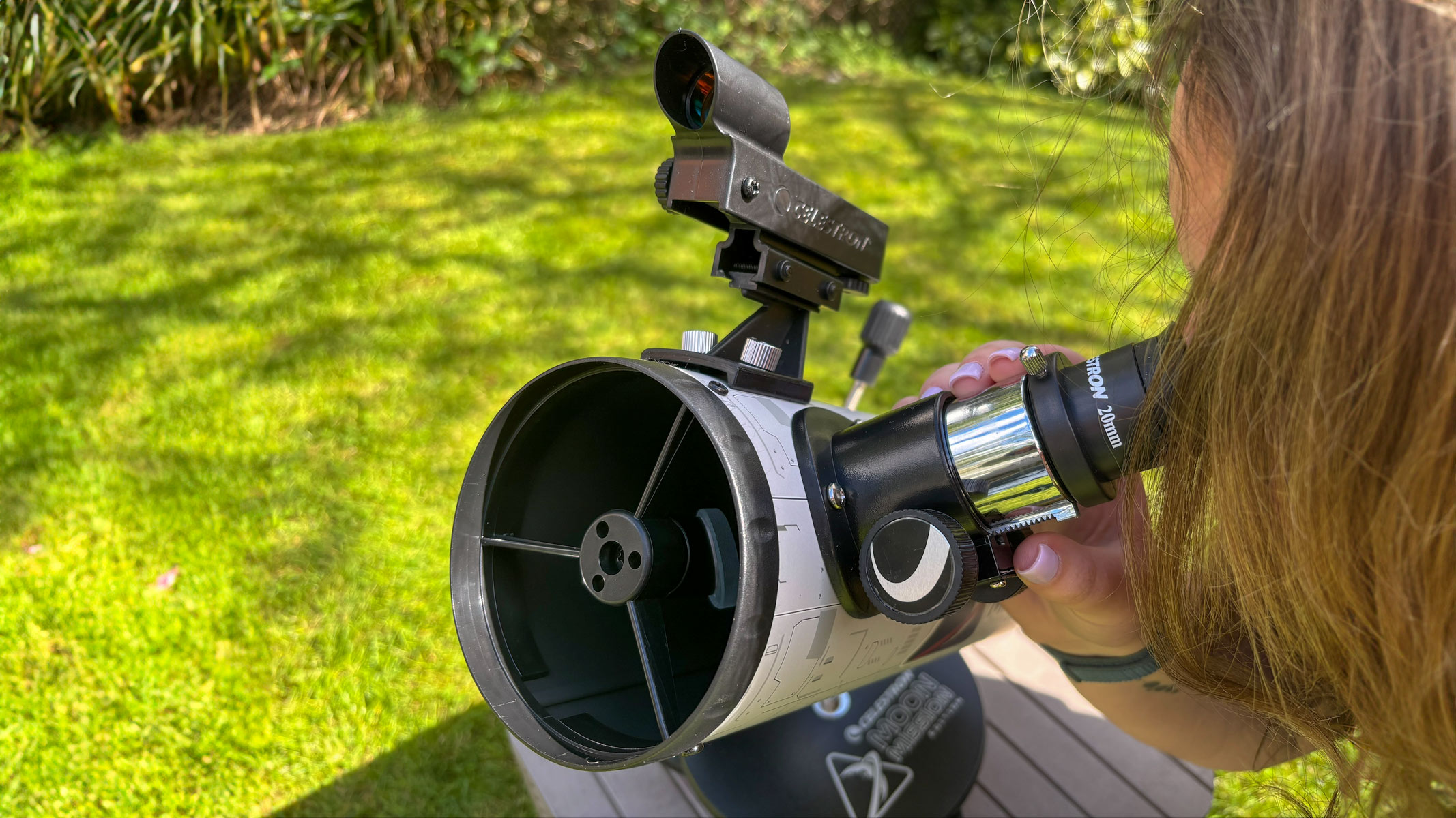 Celestron Moon Mission 100mm tabletop Dobsonian review 2 MyCelestialApp A woman looking through the eyepiece of the Celestron Moon Mission 100mm Tabletop Dobsonian with grass in the background.