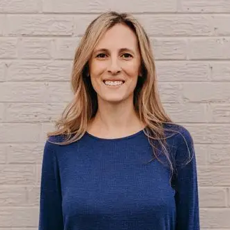 Dr Gabriela Van Sickle smiles at the camera, standing in front of a white brick wall.